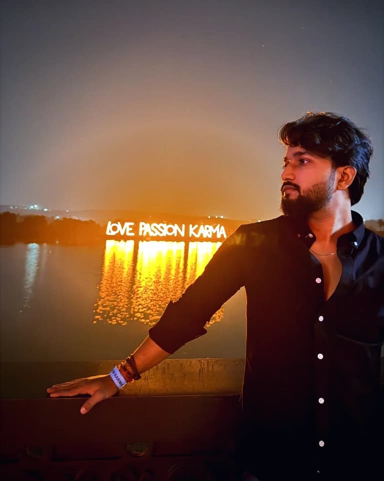 Biswa at night by a lake, with a glowing Love Passion Karma sign behind him